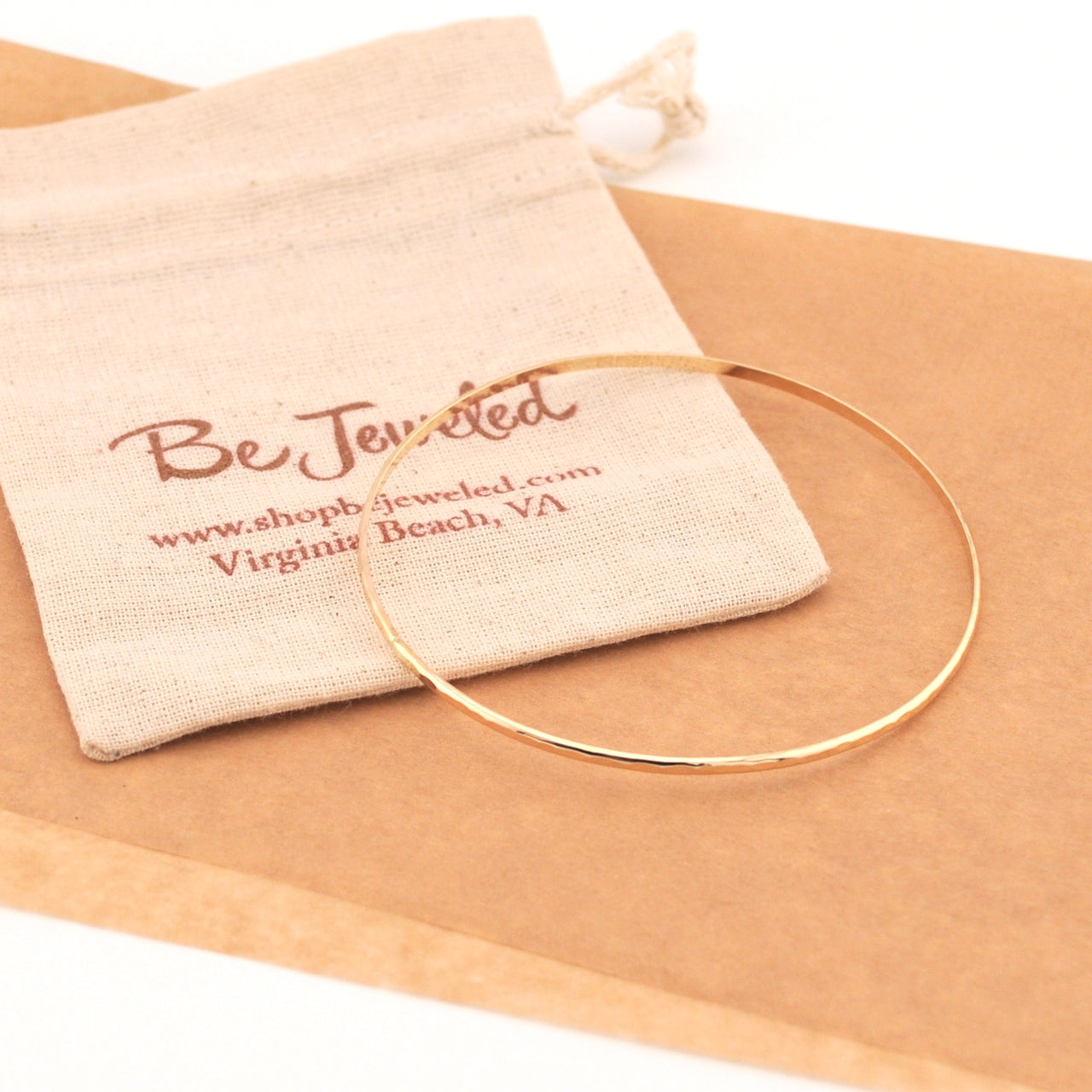 Gold bracelet on a beige fabric with 'Be Jeweled' pouch