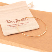 Gold bracelet on a beige fabric with 'Be Jeweled' pouch
