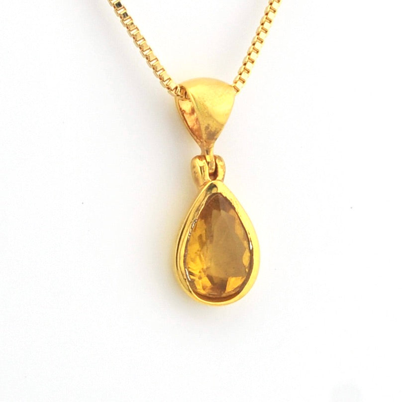 A gold pendant necklace featuring a teardrop-shaped amber gemstone, suspended from a delicate gold chain against a plain white background.