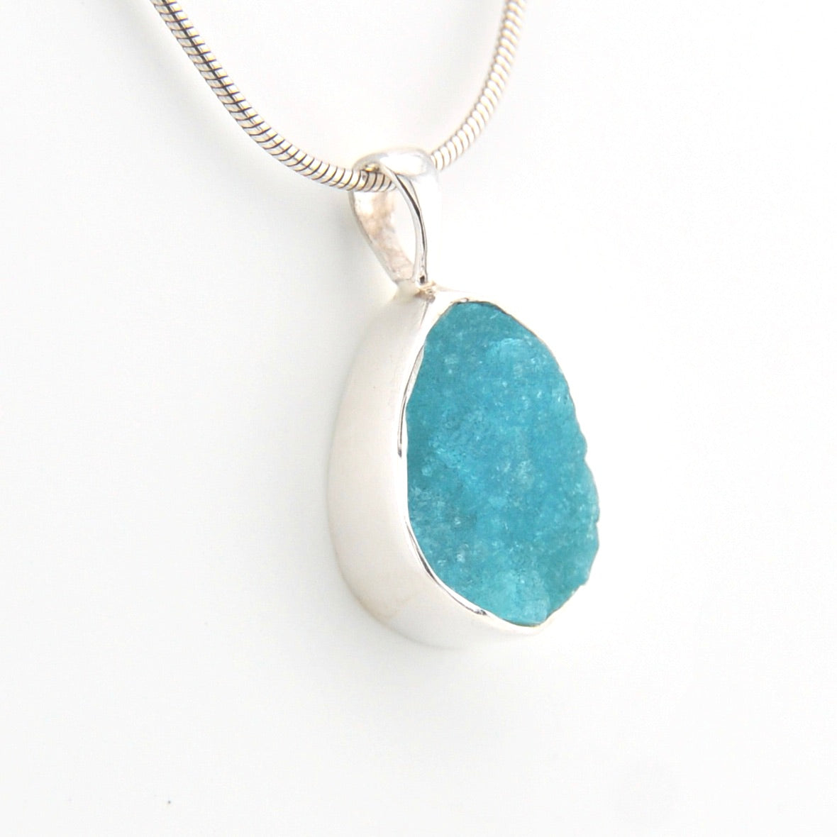Teardrop-shaped pendant with blue stone and silver chain on a white background