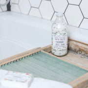 Bottle of bath salts on a wooden tray with a tiled wall background