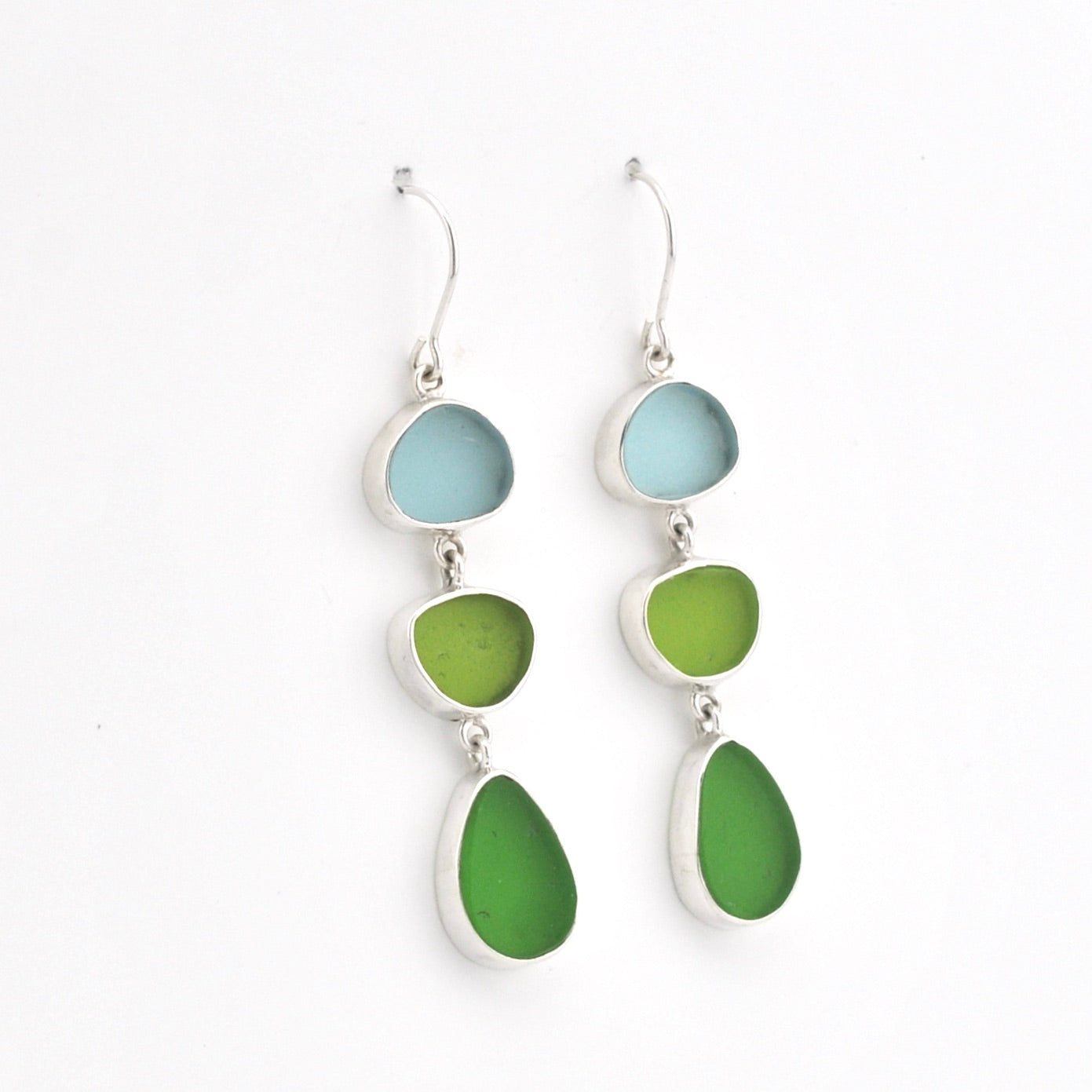 A pair of silver drop earrings featuring three stacked sea glass stones in light blue, green, and teal, shown against a plain white background.
