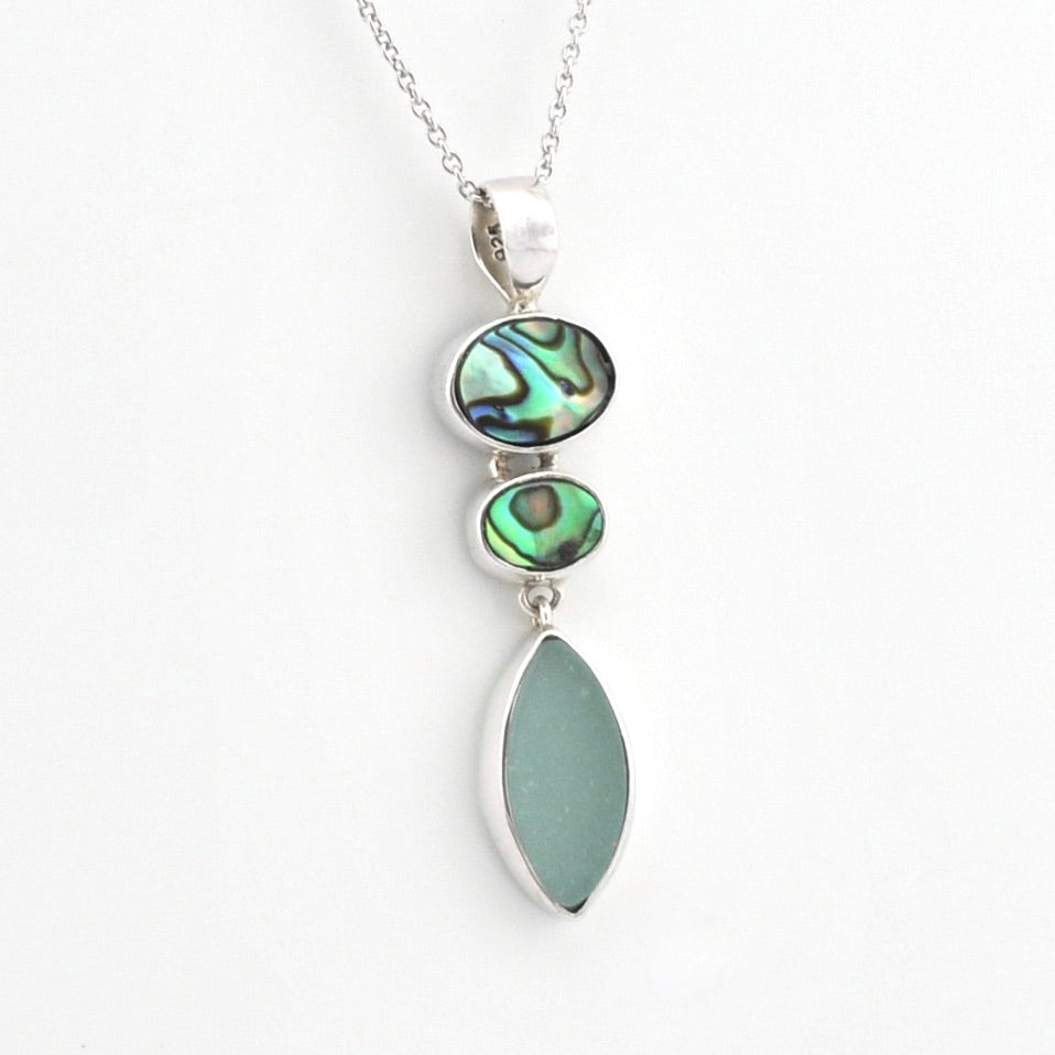 A silver pendant necklace featuring three stacked oval and teardrop-shaped iridescent green abalone shell pieces and a large smooth sea glass drop, shown on a plain white background.