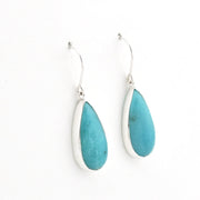A pair of silver drop earrings featuring teardrop-shaped turquoise stones, displayed against a clean white background.