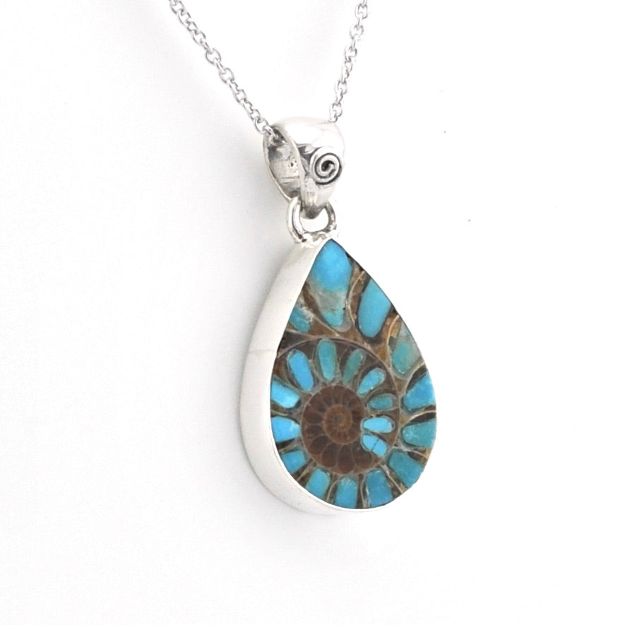 A silver teardrop pendant necklace featuring a natural ammonite fossil inlay with vibrant turquoise blue and brown segments, suspended from a delicate silver chain against a plain white background.
