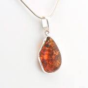 Teardrop-shaped amber pendant on a silver chain against a white background