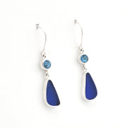 A pair of silver drop earrings featuring a small round light blue gemstone and a larger teardrop-shaped deep blue sea glass, shown on a plain white background.