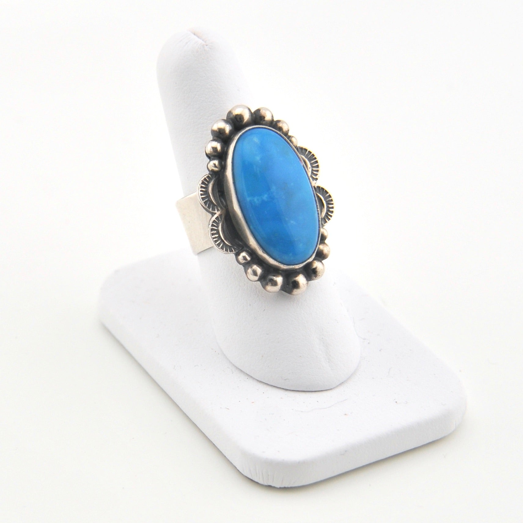 Blue stone ring with silver band on a white stand