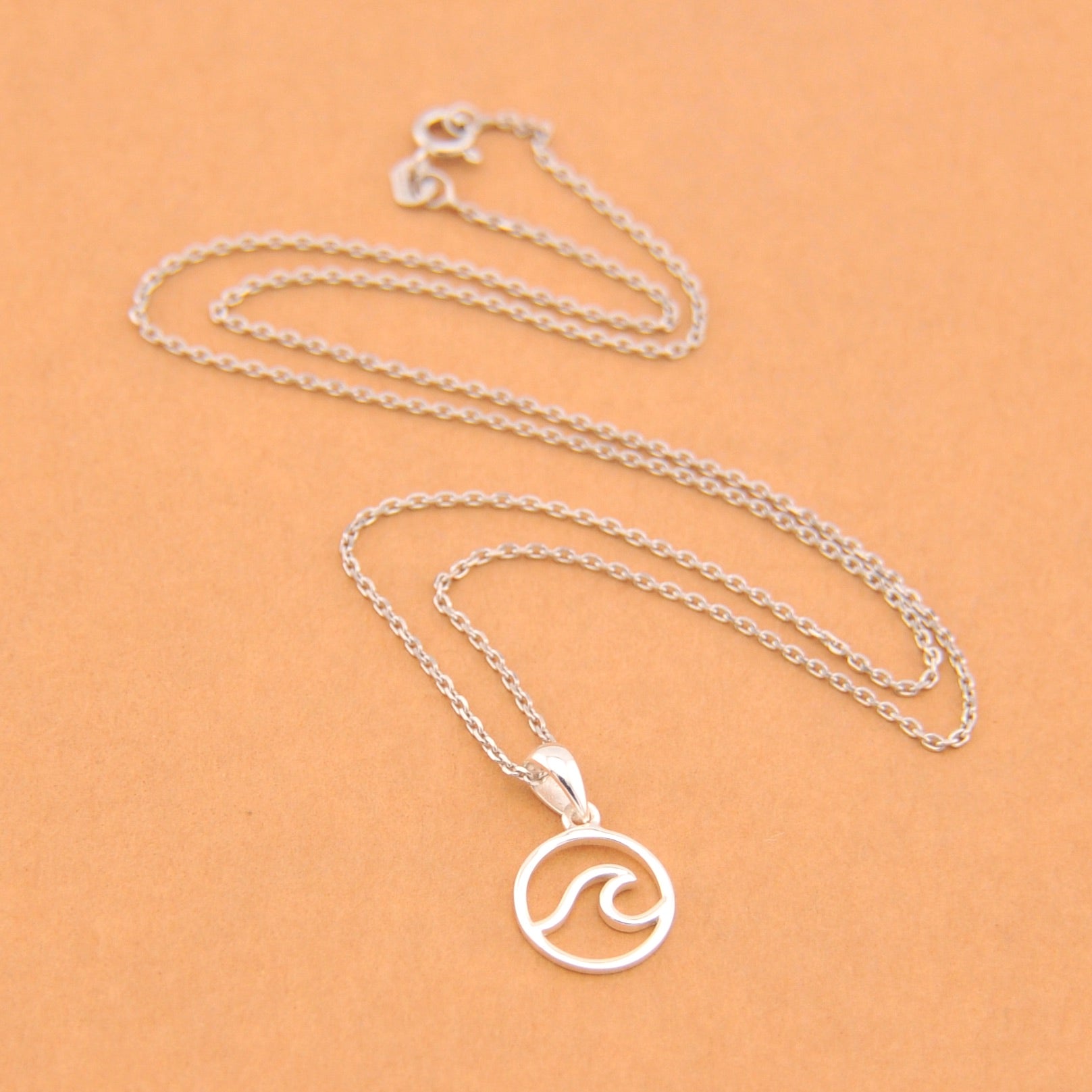 Silver necklace with a wave pendant on a beige background