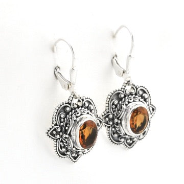 A pair of silver leverback earrings with ornate filigree details and oval amber-brown gemstones, shown on a plain white background.