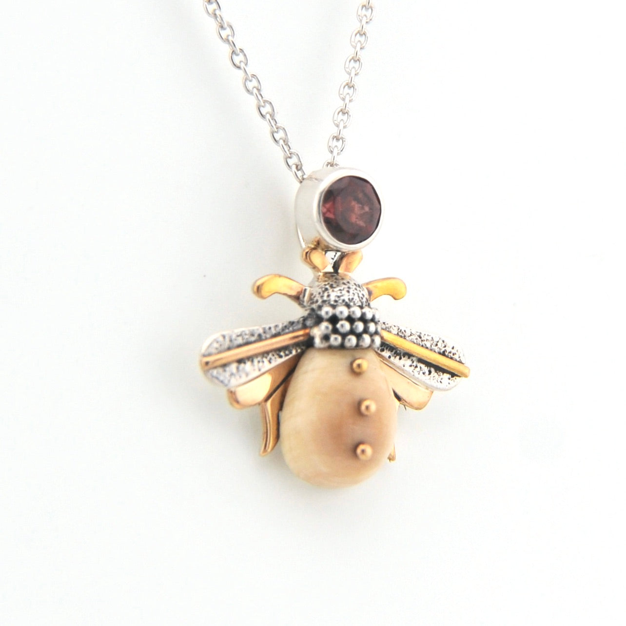 Gold and silver pendant with a red gemstone on a white background