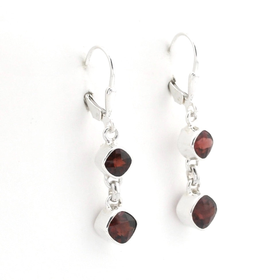 A pair of silver leverback dangle earrings featuring cushion-cut dark red garnet gemstones, shown against a plain white background.