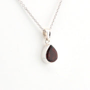 Teardrop-shaped pendant with a red gemstone on a white background