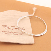 Silver bracelet on a tan surface with a branded pouch