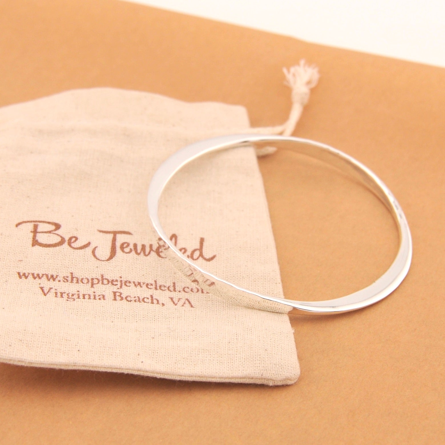 Silver bracelet on a tan surface with a branded pouch