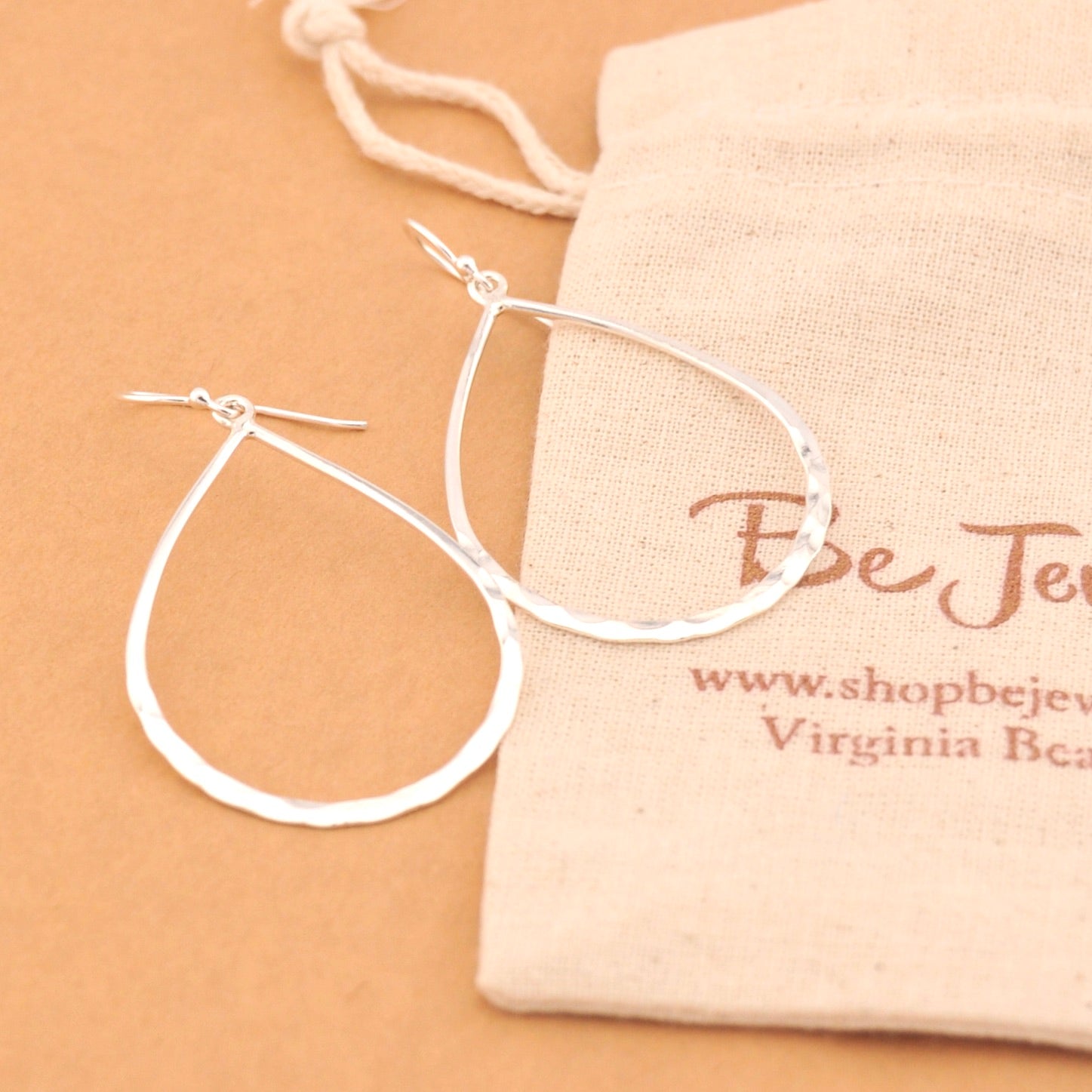Silver hoop earrings on a beige surface with a branded jewelry bag.