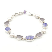 A sterling silver bracelet featuring alternating oval and heart-shaped bezel-set sea glass, including lavender-blue patterned porcelain and pearl on a white background.