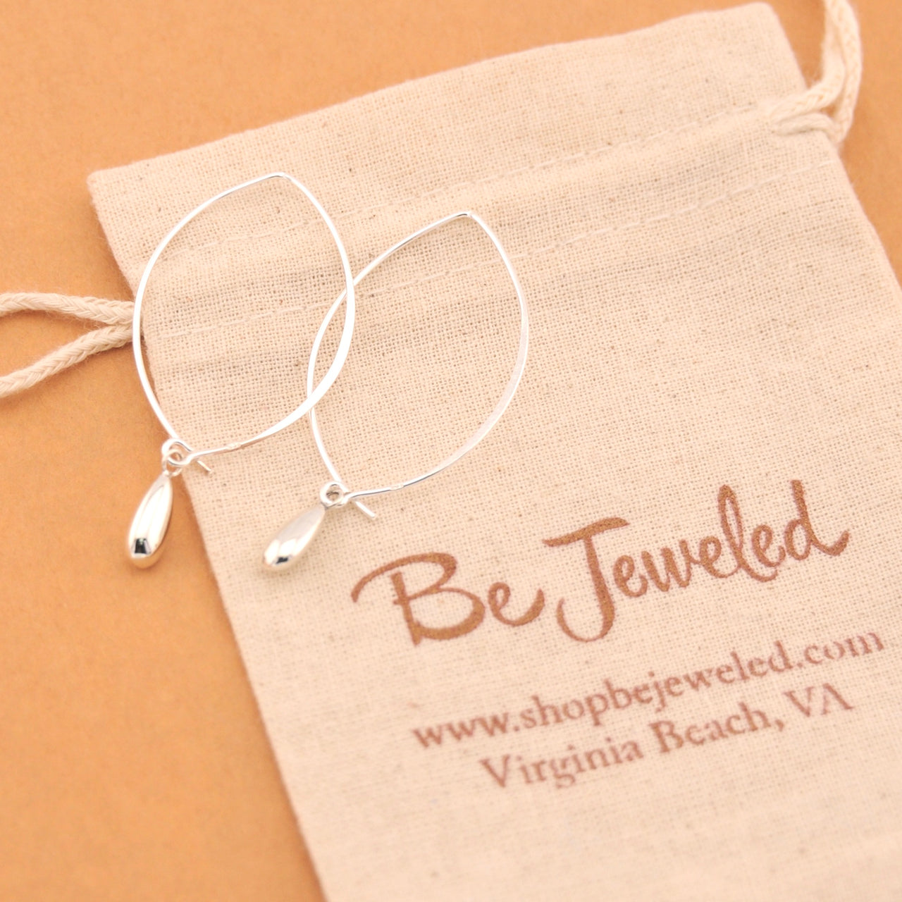 Silver hoop earrings on a 'Be Jeweled' branded pouch with a beige background