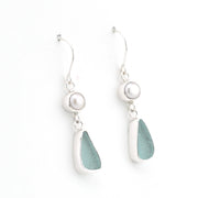 A pair of silver drop earrings featuring a white pearl, a teardrop-shaped piece of sea glass, and a small silver bead, shown on a plain white background.