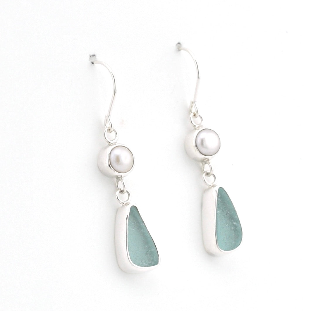 A pair of silver drop earrings featuring a white pearl, a teardrop-shaped piece of sea glass, and a small silver bead, shown on a plain white background.