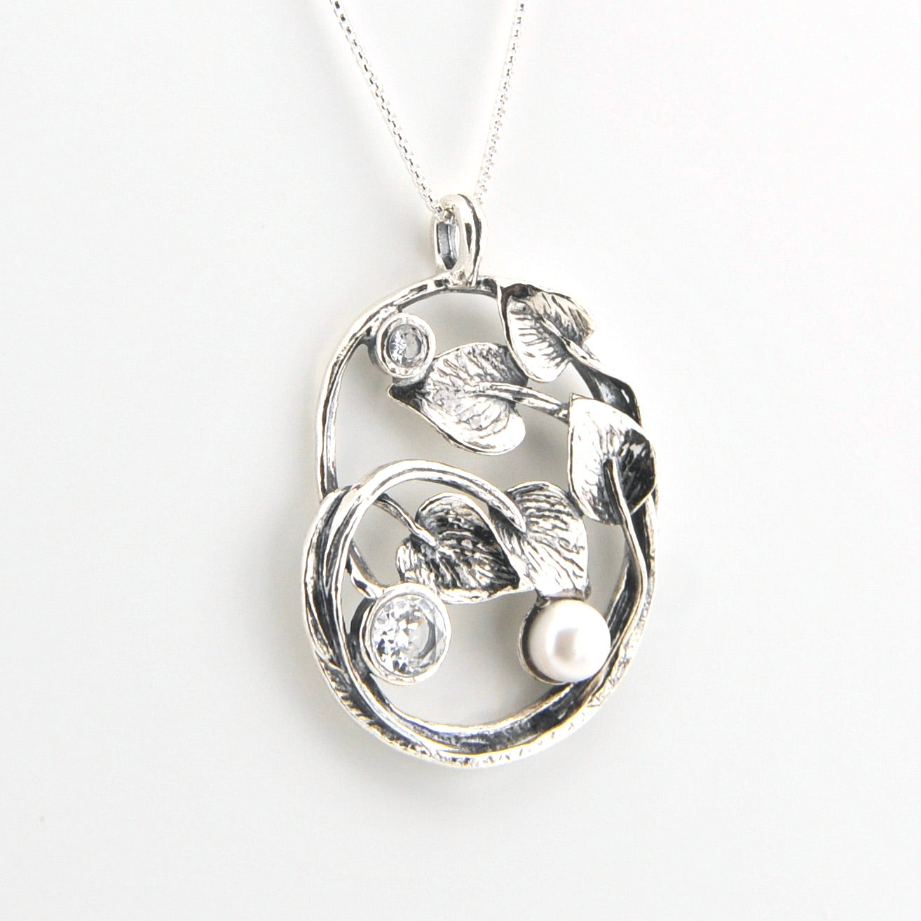 Silver pendant with leaf designs and a pearl on a white background