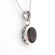 A silver pendant necklace featuring an oval dark brown gemstone in an ornate, textured silver bezel setting, suspended from a silver chain against a plain white background.