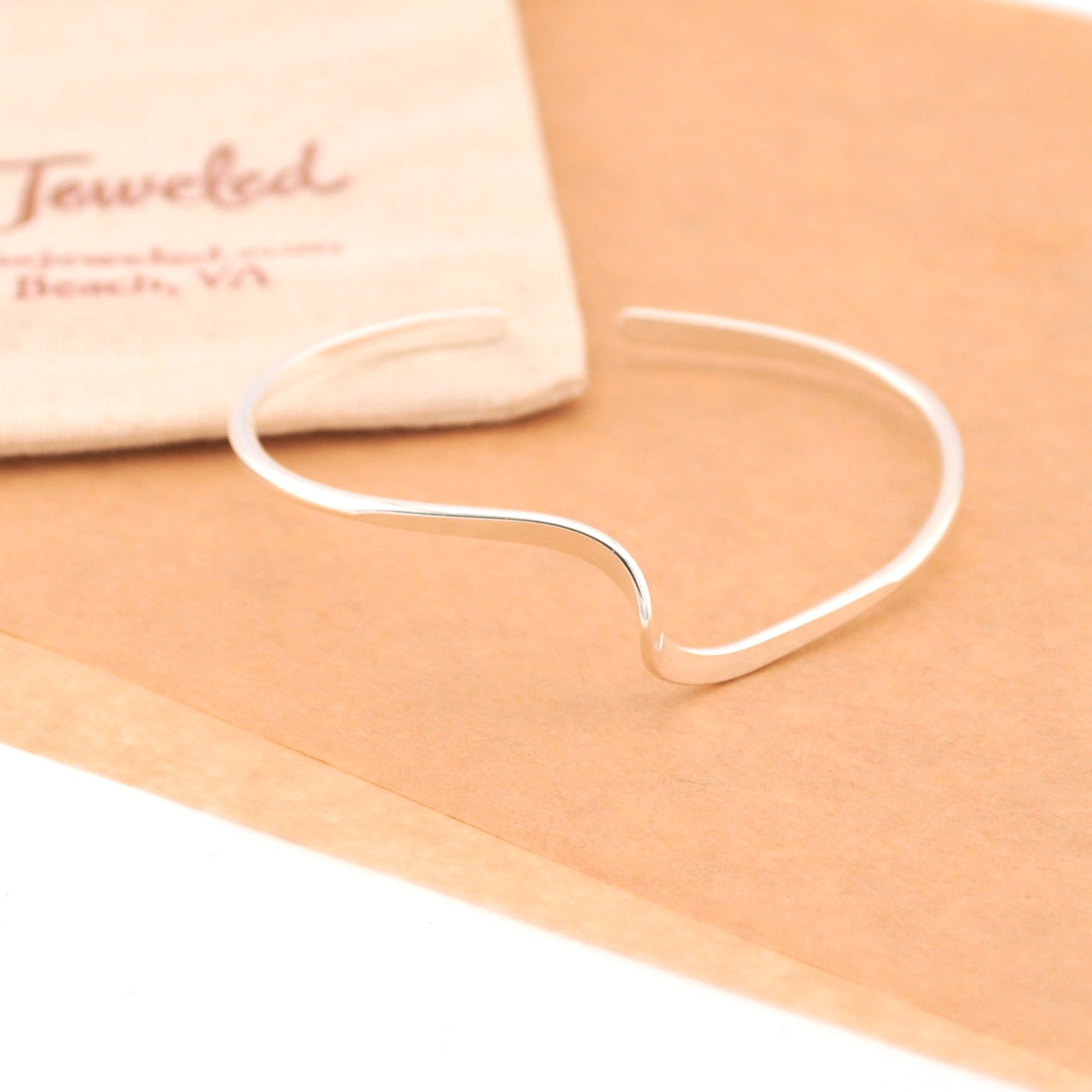 Silver bangle on a beige surface with 'Jeweled' branding in the background