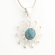 Silver sun-shaped pendant with a turquoise center on a white background