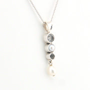 Silver necklace with three stones and a pearl on a white background