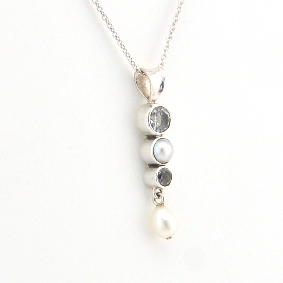 Silver necklace with three stones and a pearl on a white background