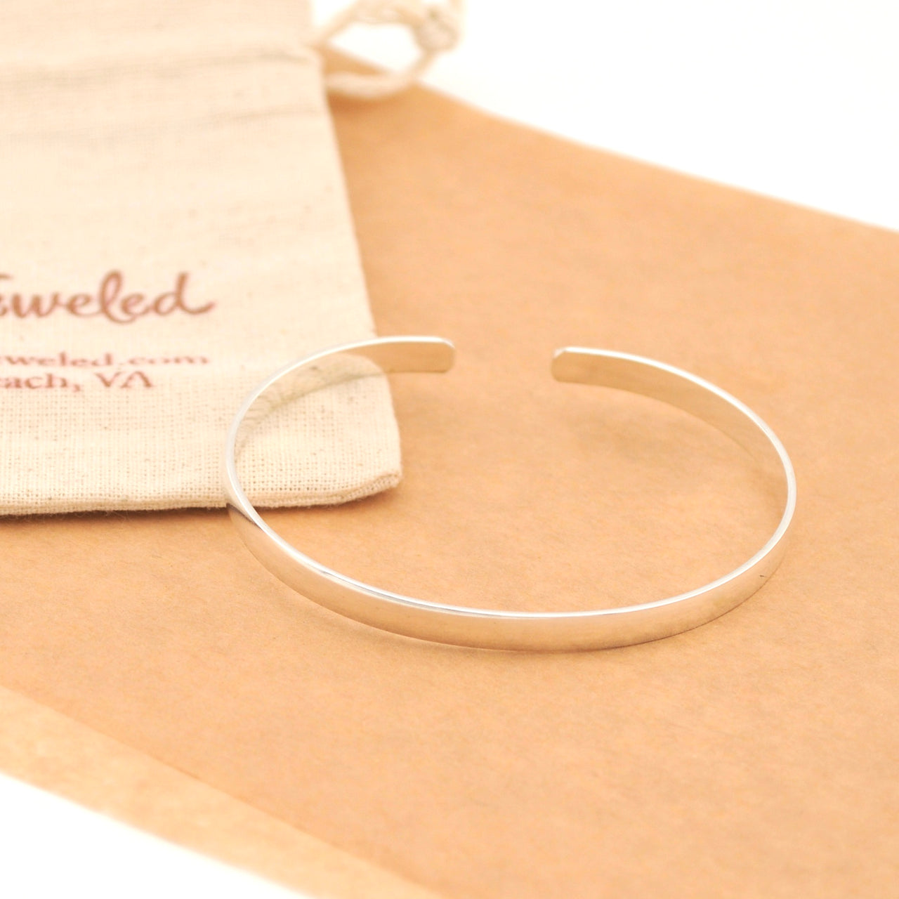 Silver bracelet on a beige surface with a branded pouch in the background