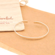 Silver bracelet on a beige surface with a branded pouch in the background