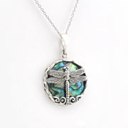 A silver dragonfly pendant necklace featuring a detailed dragonfly design over a round iridescent abalone shell background, suspended from a delicate silver chain on a white background.