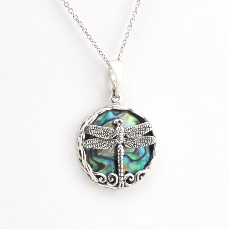 A silver dragonfly pendant necklace featuring a detailed dragonfly design over a round iridescent abalone shell background, suspended from a delicate silver chain on a white background.