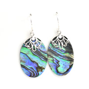 A pair of dangling earrings with oval abalone shell showing blue, green, and purple iridescence, suspended from silver filigree hoops on silver fishhook wires, set against a plain white background.