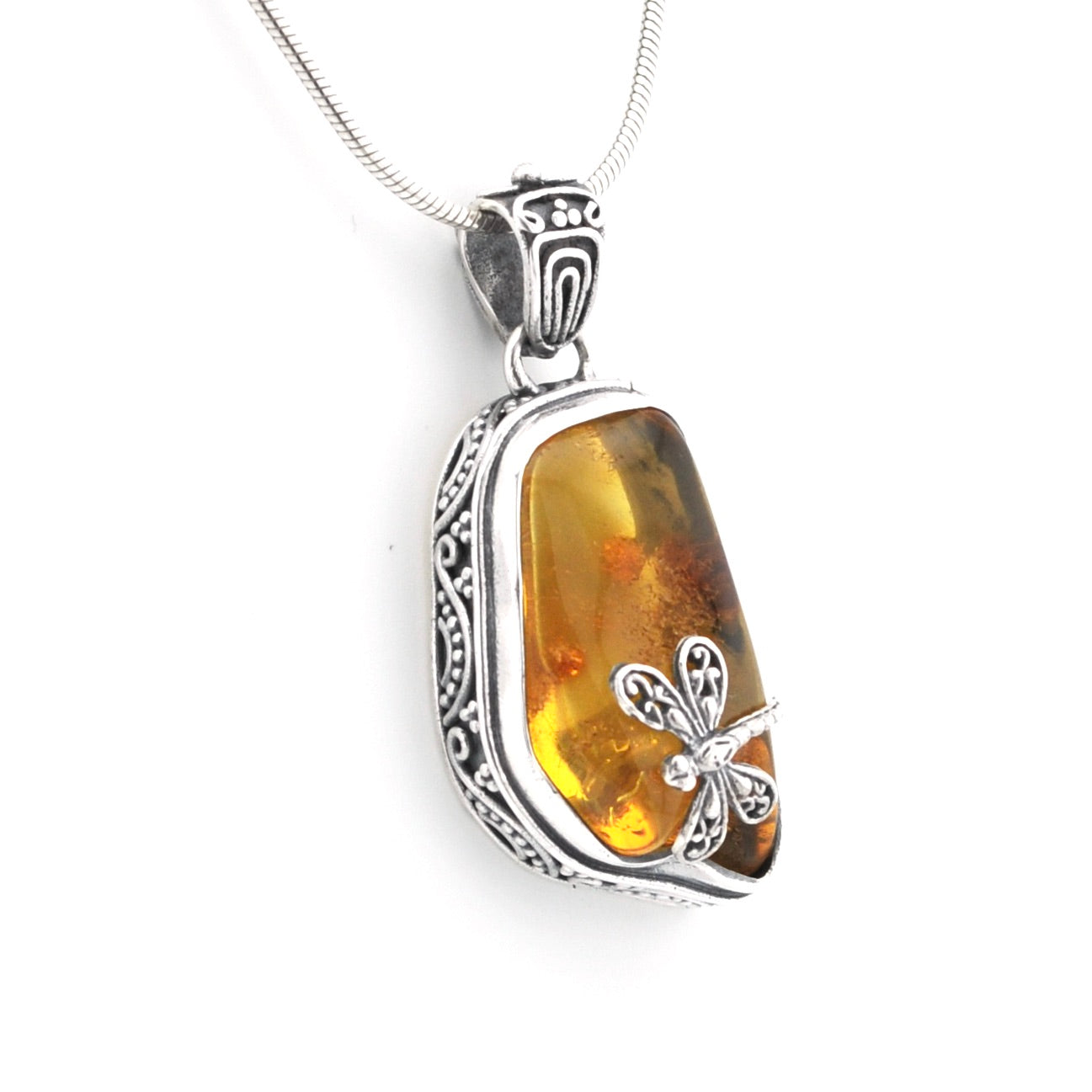 A silver pendant necklace featuring a polished amber stone with dragonfly inclusions, set in an ornate silver bezel with a silver chain on a white background.