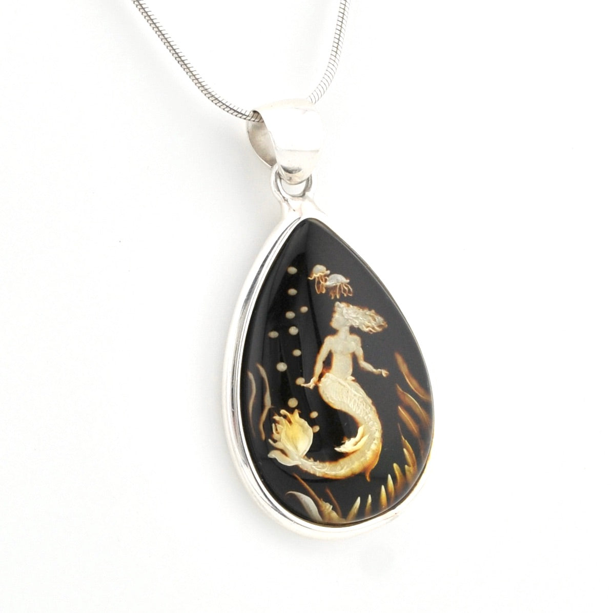 A silver teardrop pendant necklace featuring a black background with a gold mermaid and sea creature design, suspended from a silver chain on a white background.