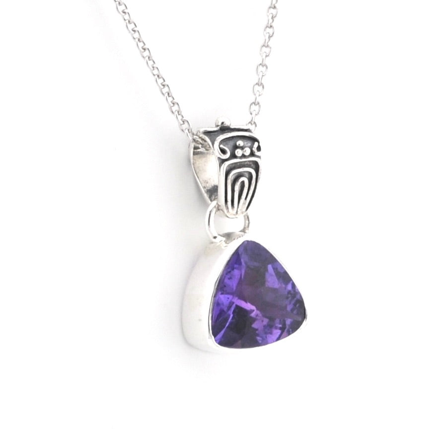 A silver pendant necklace featuring a triangular purple amethyst gemstone in a bezel setting, suspended from a silver chain with a decorative engraved bail.