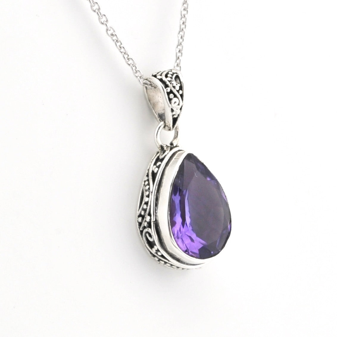 A silver teardrop pendant necklace with an ornate filigree border and a faceted purple gemstone, shown on a plain white background.