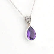 A silver teardrop pendant necklace featuring a faceted purple gemstone, suspended from a delicate silver chain against a plain white background.