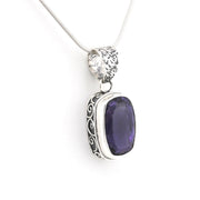 A silver pendant necklace featuring a rectangular purple gemstone with ornate silver filigree detailing on the sides, suspended from a silver snake chain against a plain white background.
