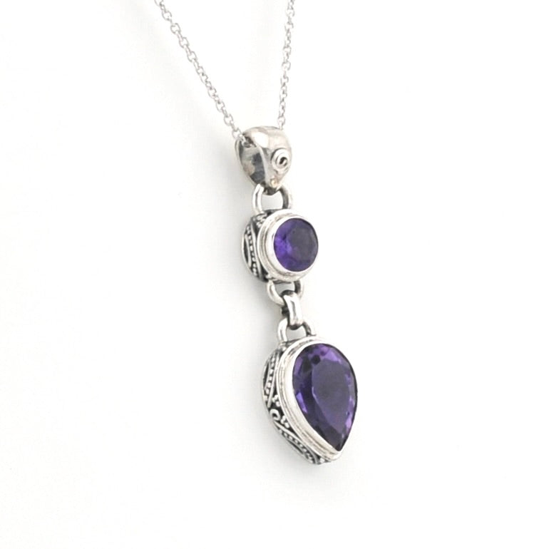 A silver pendant necklace featuring a teardrop-shaped purple gemstone and a smaller oval purple gemstone, displayed on a clean white background.