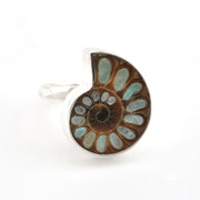 A silver ring featuring a polished spiral ammonite fossil inlay with brown and light blue-green segments, set against a plain white background.