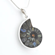 A silver pendant necklace featuring a polished cross-section of an ammonite fossil with iridescent inclusions, suspended from a silver snake chain against a white background.