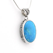 An oval pendant necklace featuring a vibrant blue turquoise stone set in an ornate silver filigree bezel, suspended from a silver snake chain against a plain white background.
