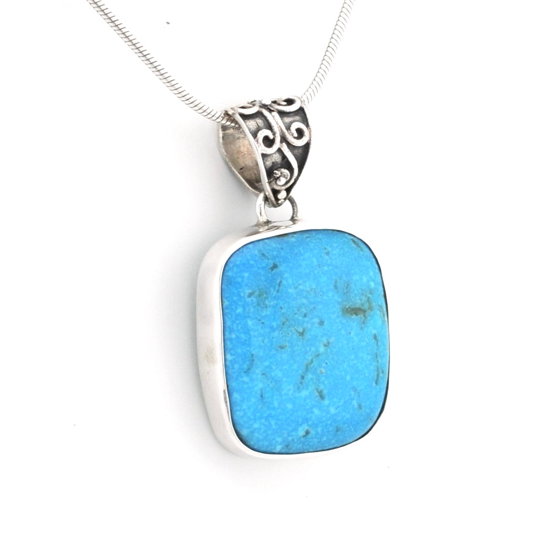 A silver pendant necklace featuring a rectangular turquoise-blue stone with rounded corners, set in a polished silver bezel and suspended from a silver chain with an ornate scrollwork bail.