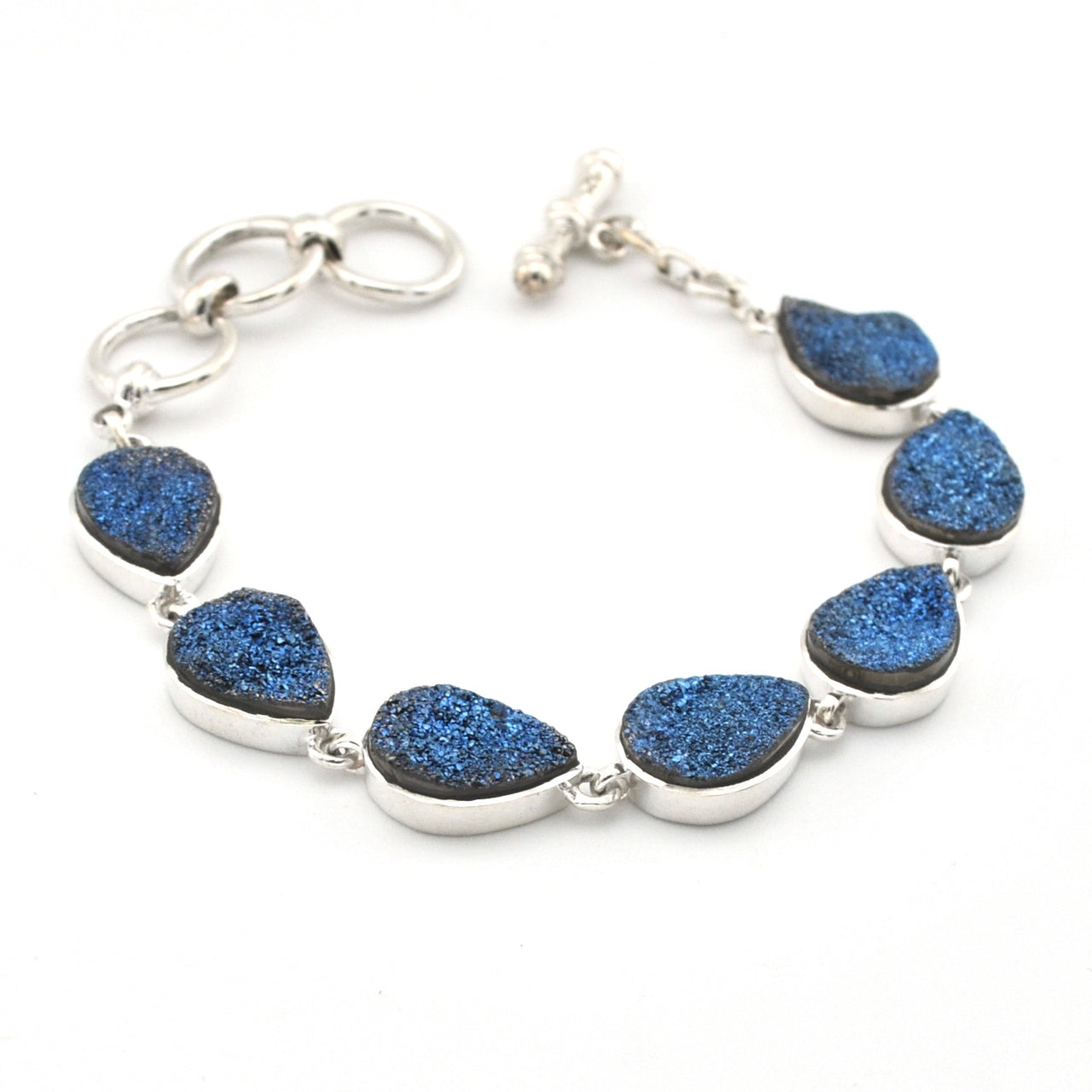 A silver-toned bracelet featuring seven teardrop-shaped blue glitter stones set in silver bezels, displayed on a clean white background.