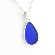 A teardrop-shaped cobalt blue glass pendant necklace with a silver bezel and chain, shown on a plain white background.