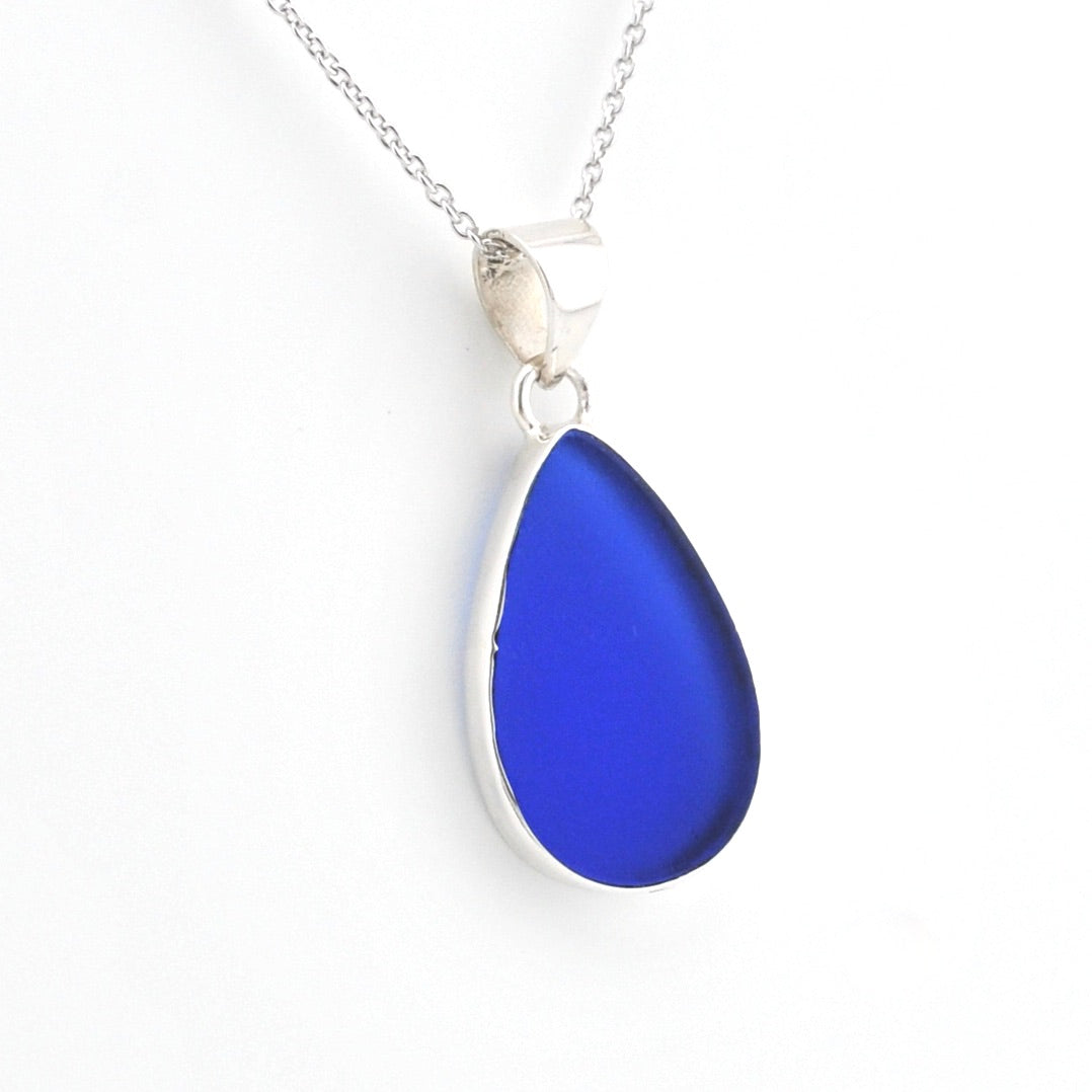 A teardrop-shaped cobalt blue glass pendant necklace with a silver bezel and chain, shown on a plain white background.