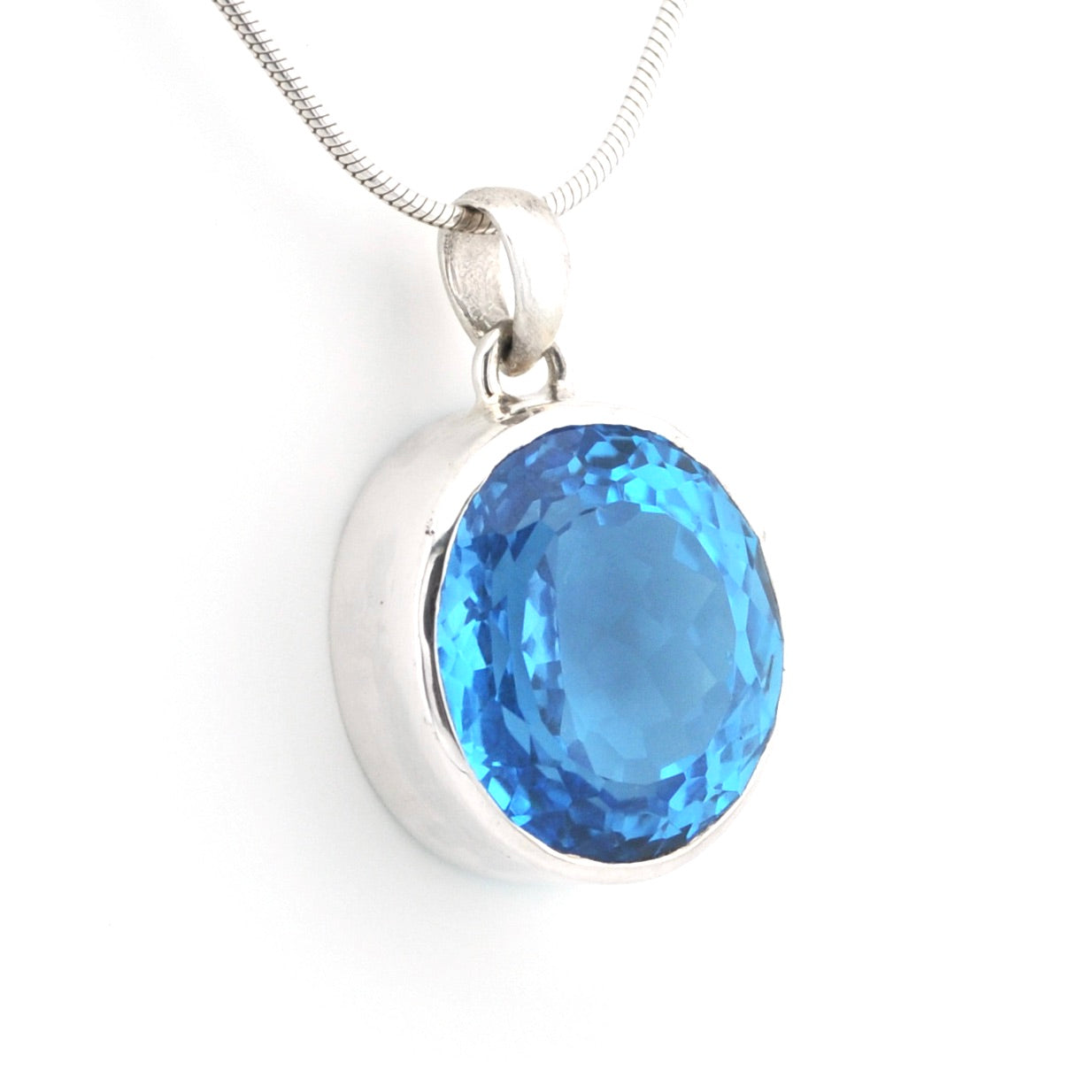 A silver pendant necklace featuring a large, oval-cut light blue gemstone in a polished silver bezel setting, suspended from a silver snake chain against a white background.